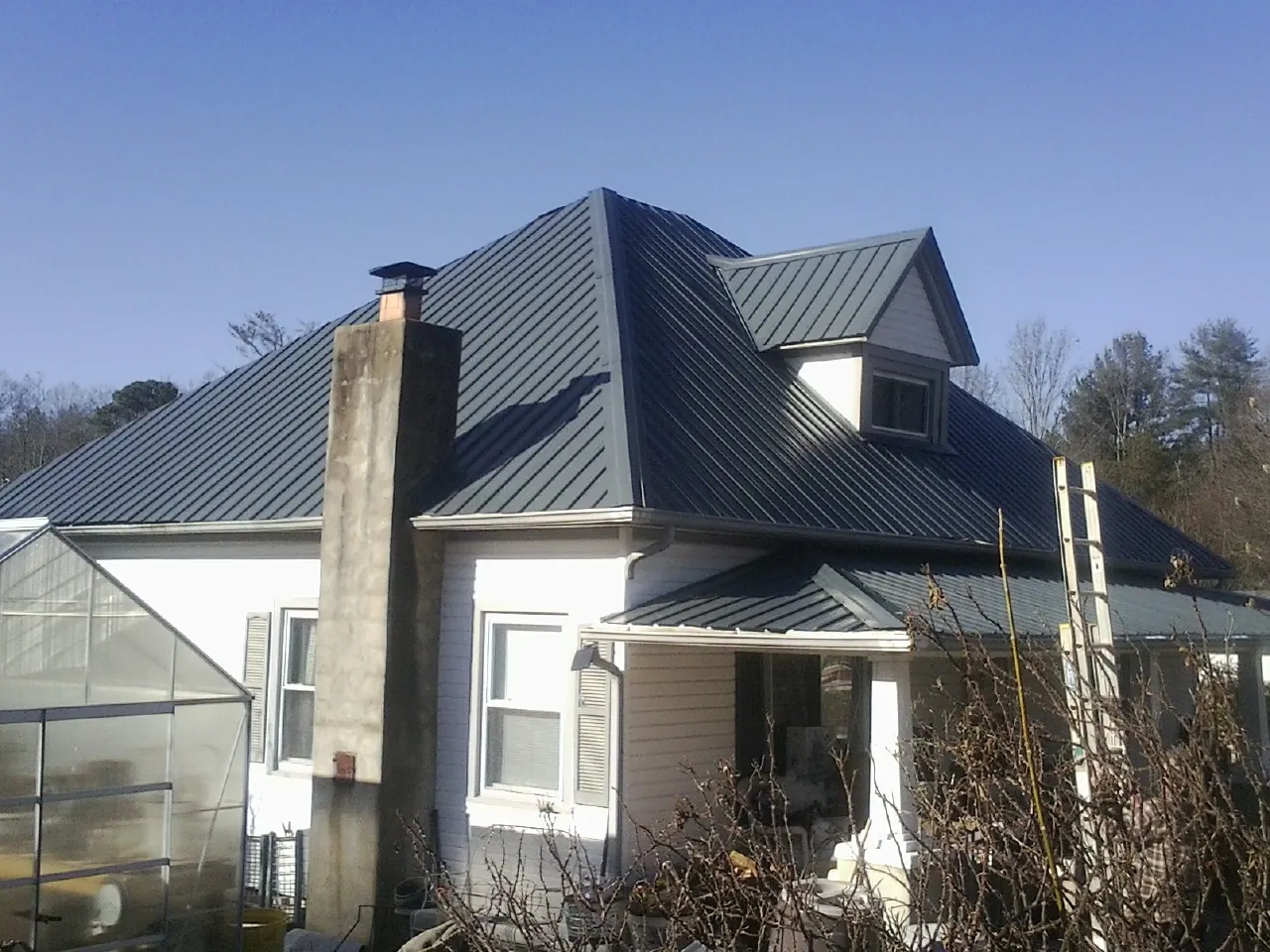 Dark blue standing seam metal roof on a white farmhouse with dormer — Slate & Tile Roof Repair by Roofing Brothers in Renner