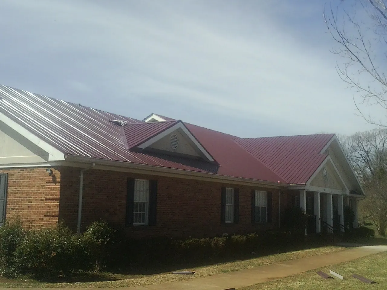 Red metal roof with gabled entries on a long brick building, from a Hail Damage Roof Repair job in Renner