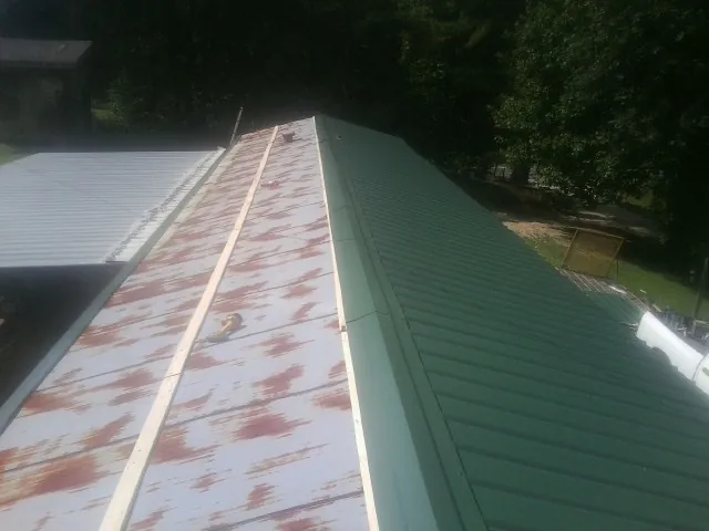 Old rusted panels beside newly installed green metal roofing — Wind Damage Roof Repair by Roofing Brothers in Renner
