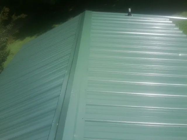 New green metal panels meeting at the ridge of a roof — Flat Roof Repair work by our crew in Renner