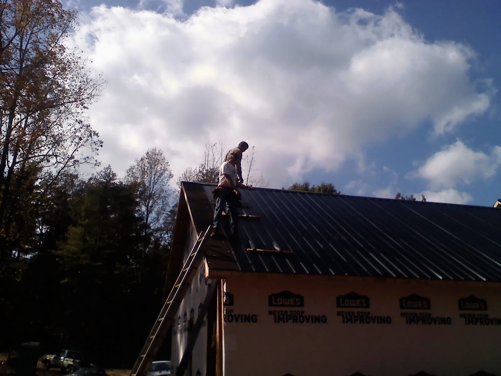 Roofer fastening dark metal panels high against a cloudy sky, from a Roof Inspection job in Renner