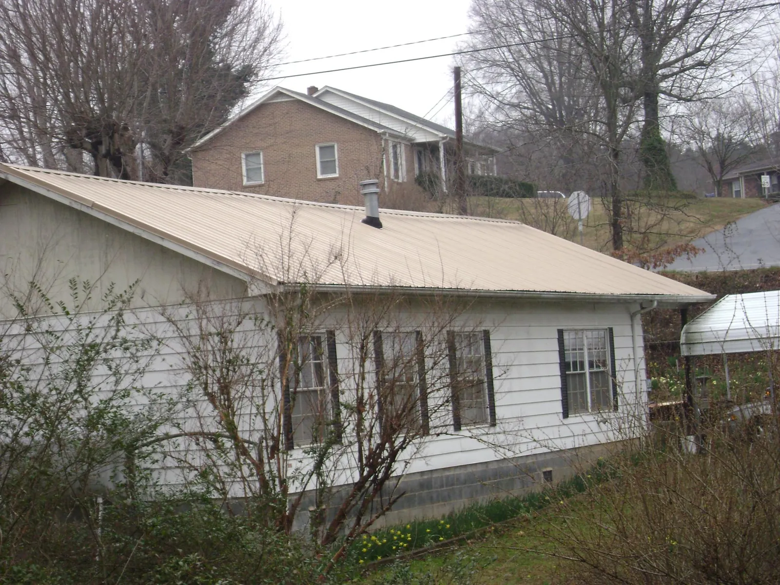 Tan metal roof on a white sided house set into a hillside — Commercial Roofing by Roofing Brothers in Renner