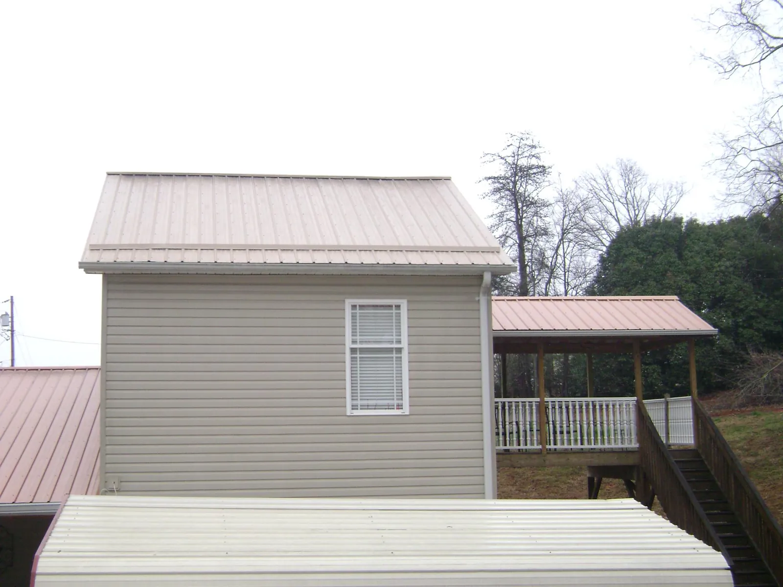 Tan metal roofs on a two story addition and attached porch, from a Roof Replacement job in Renner